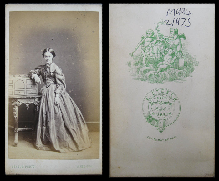 Carte de visite, 1860s, unknown lady in criniline, plain background. Reverse has  garter design and engraving of globe and cherubs. Town name spelled "Wisbech".